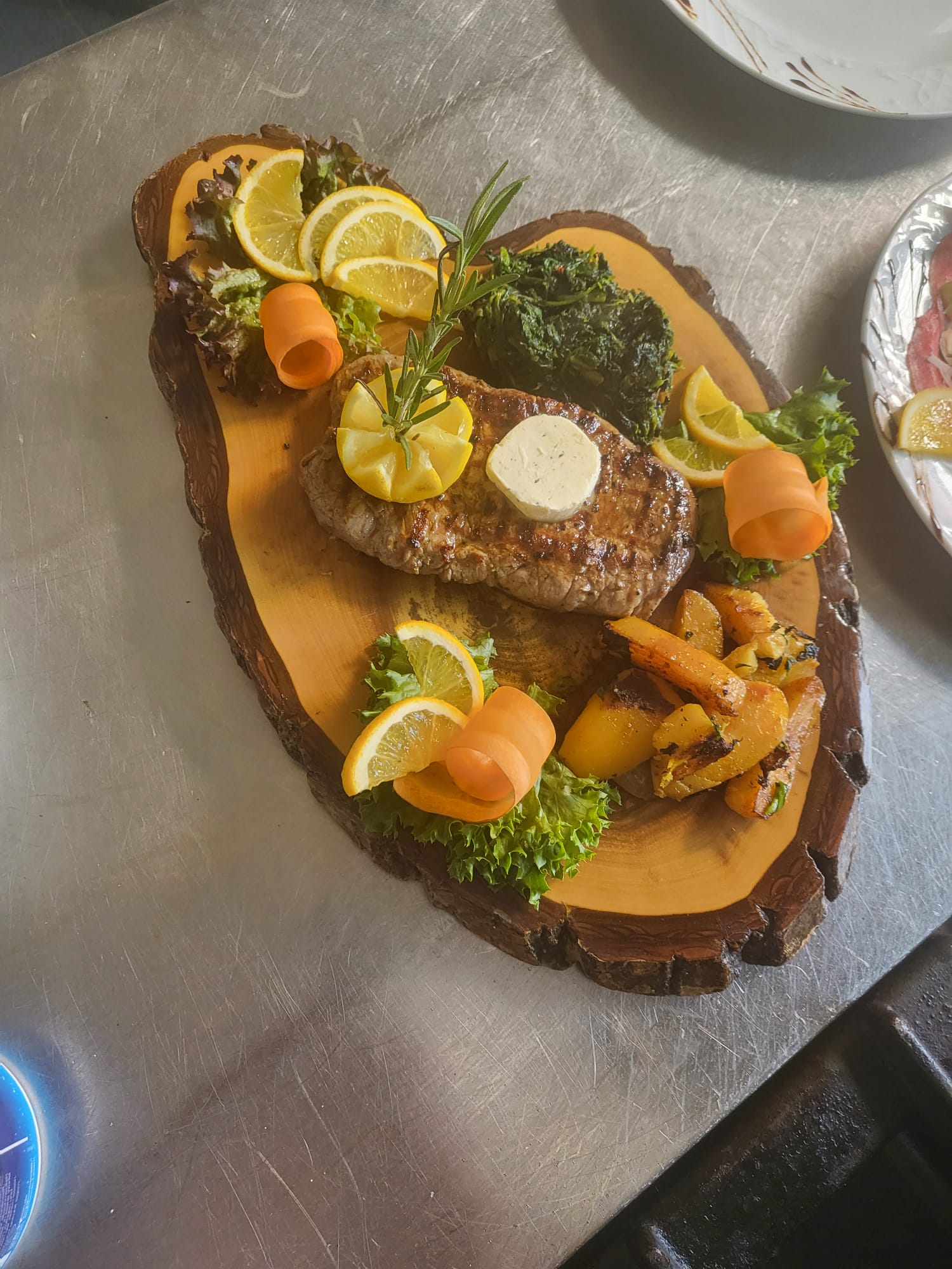 Bistecca Paganini — Rumpsteak mit Kräuterbutter, Pesto, Rosmarin, Karotten und Salatbouquet auf Holzbrett